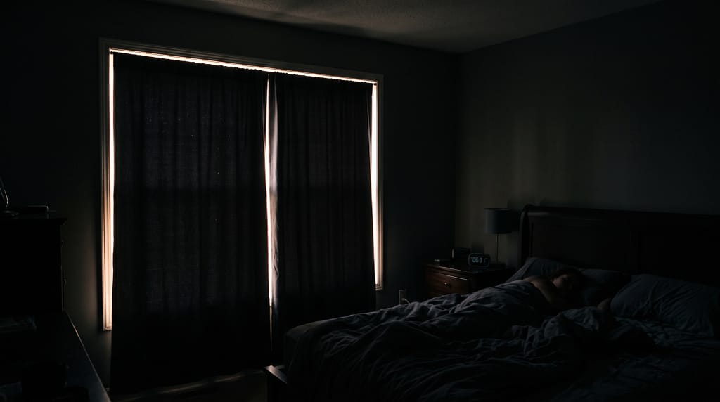 Blackout curtains in a bedroom blocking morning light - room in near-complete darkness with only thin edge light visible