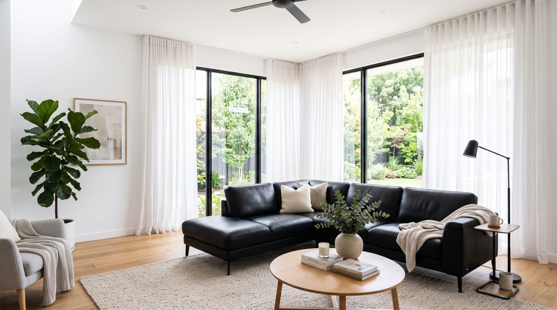 Black sofa in a bright white living room with large windows and sheer curtains